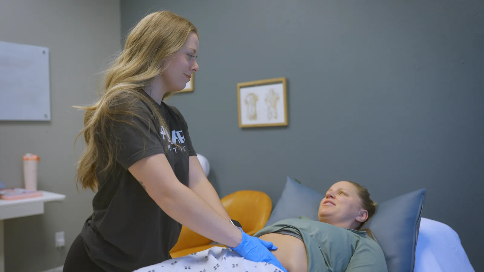A pelvic health physical therapist assessing a patient's abdomen in a private treatment room